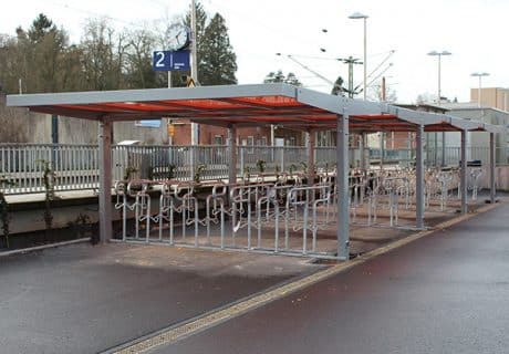 Eine Fahrradüberdachung mit mehreren Fahrradbügeln und rotem Dach an einem Bahnhof
