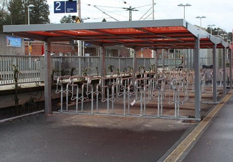 Eine Fahrradüberdachung mit mehreren Fahrradbügeln und rotem Dach an einem Bahnhof