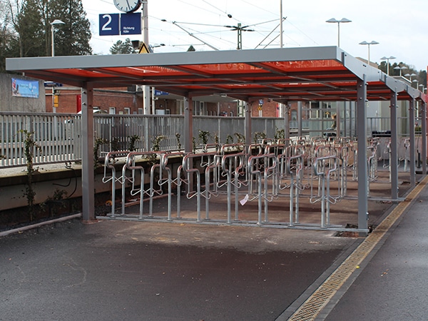 Eine Fahrradüberdachung mit mehreren Fahrradanlehnbügeln und rotem Dach an einem Bahnhof