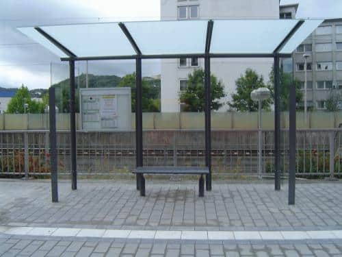 Eine gläserne Wartehalle mit Bank an einem Bahnsteig