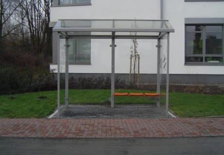 Eine graue zweifeldrige Wartehalle mit rechtwinkligen Dachscheiben am Straßenrand