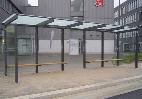 Eine graue fünffeldrige Wartehalle mit zwei Holzbänken über zwei Felder