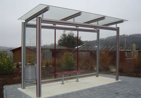 Eine graue dreifeldrige transportable Wartehalle mit oberflächenstrukturierter Betonbodenplatte mit Scheibendekor und Drahtgittersitzbank