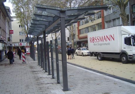 Eine Fahrradüberdachung am Straßenrand vor mehreren Geschäften