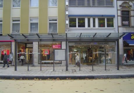 Eine Fahrradüberdachung am Straßenrand vor mehreren Geschäften