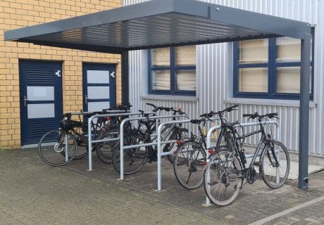 Eine Fahrradüberdachung mit mehreren Fahrradanlehnbügeln vor einer Metallwand
