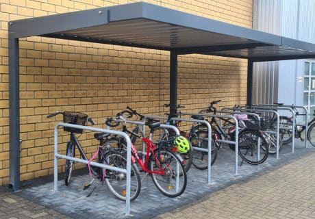 Eine Fahrradüberdachung mit mehreren Fahrradanlehnbügeln vor einer Steinwand
