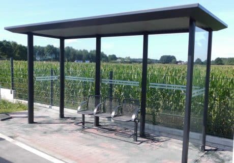 Eine graue Wartehalle mit Drahtgittersitzbank inklusive Rückenlehne und Blindentaskleiste