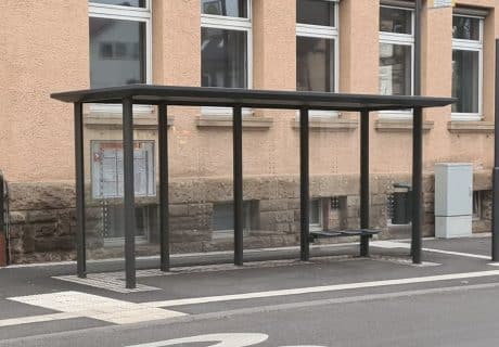 Eine graue vierfeldrige Wartehalle vor einem beigefarbenen Gebäude