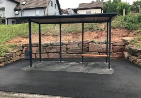 Eine graue dreifeldrige Wartehalle mit Holzsitzbank