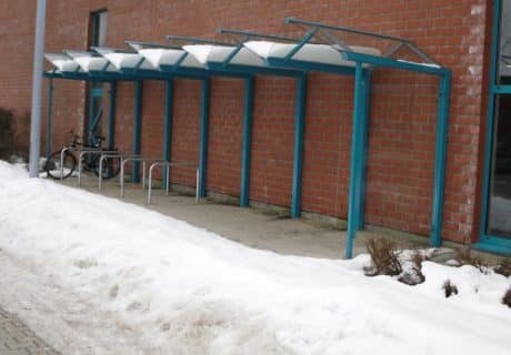 Eine Fahrradüberdachung, auf der sich Schnee gesammelt hat, mit mehreren Fahrradanlehnbügeln