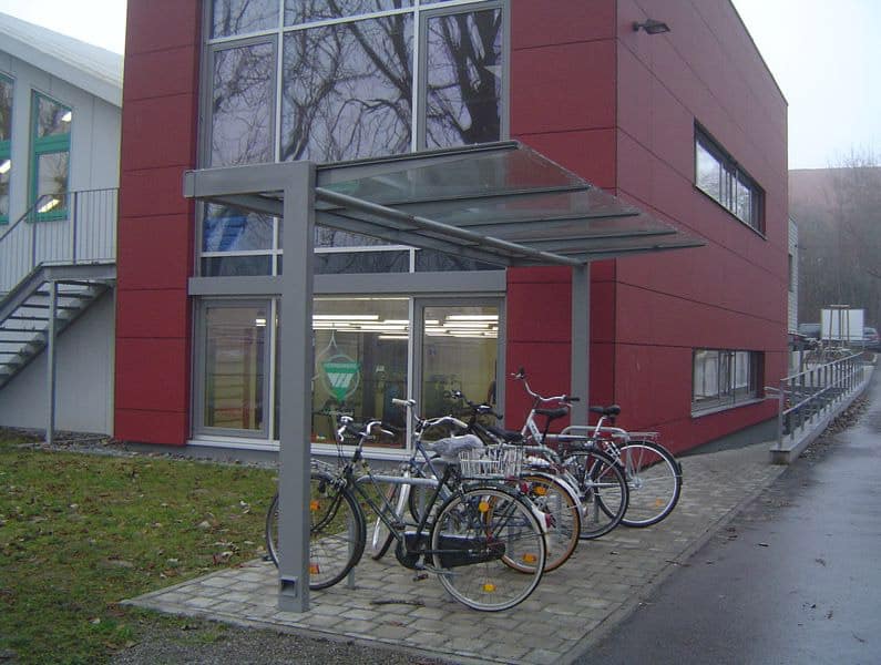 Eine Fahrradüberdachung am Straßenrand neben einem roten Gebäude