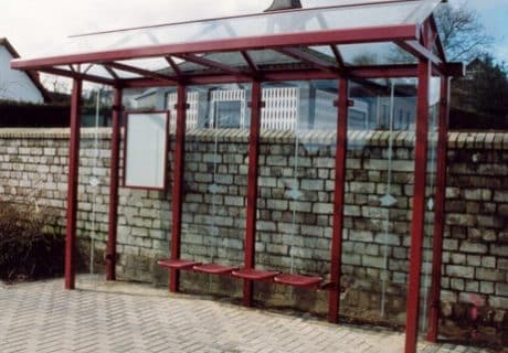 Eine rote vierfeldrige Wartehalle mit rechtwinkligen Dachscheiben am Straßenrand